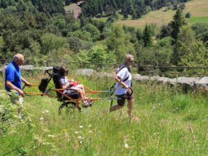 Una persona che percorre un sentiero accessibile con degli accompagnatori e una joelette